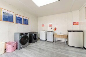 A laundry room with multiple washing machines, a dryer, a sink, and a trash bin. - Ramada by Wyndham Zhangjiajie (Zhangjiajie)