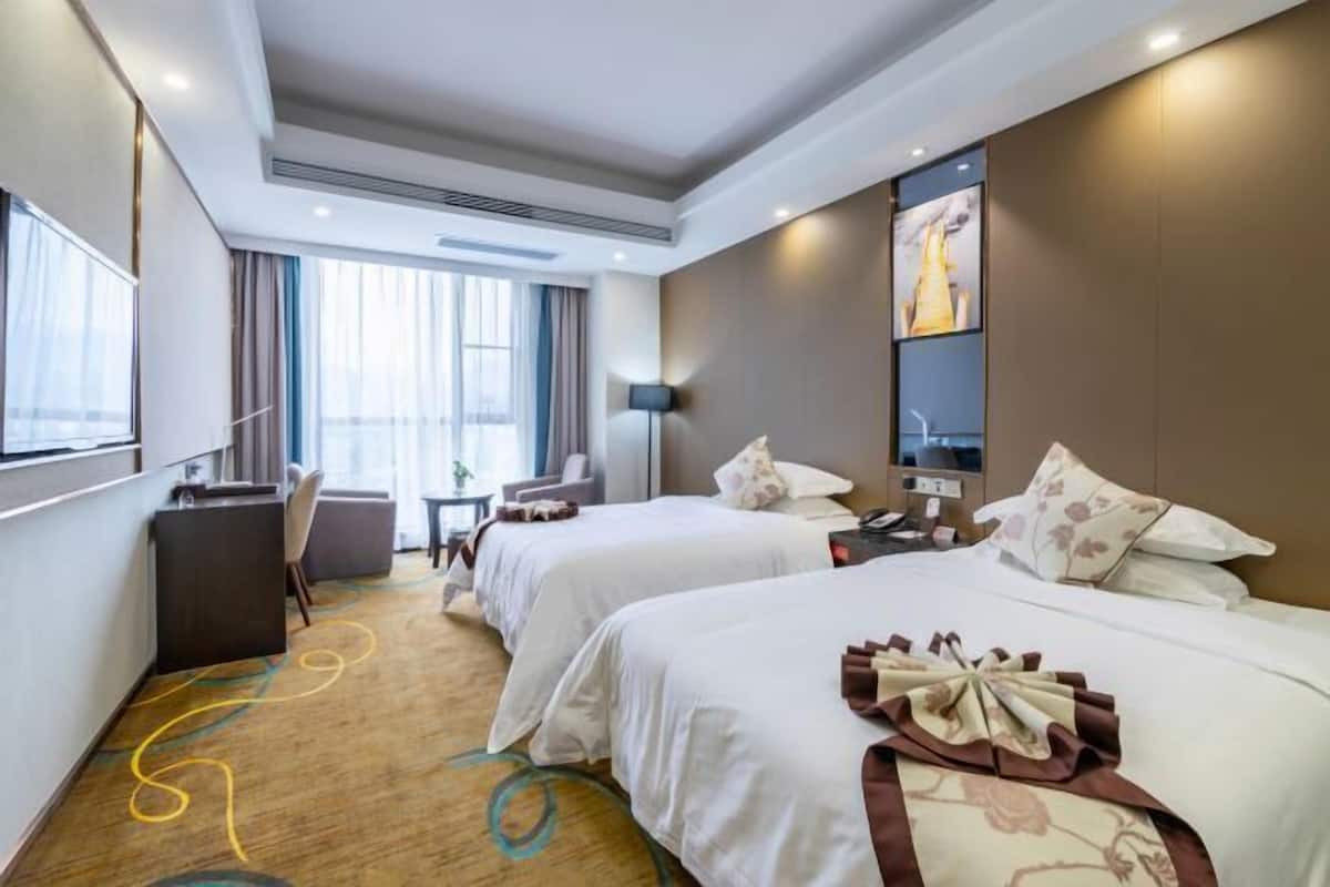 Ein Hotelzimmer mit zwei Betten, einem Schreibtisch, einem Stuhl und einem großen Fenster.
