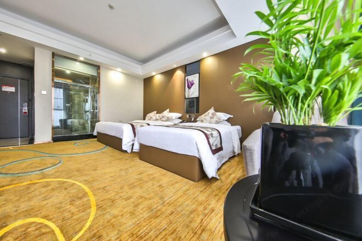 Ein Hotelzimmer mit zwei Betten, einem großen Spiegel, einer Zimmerpflanze und einem Flachbildfernseher.