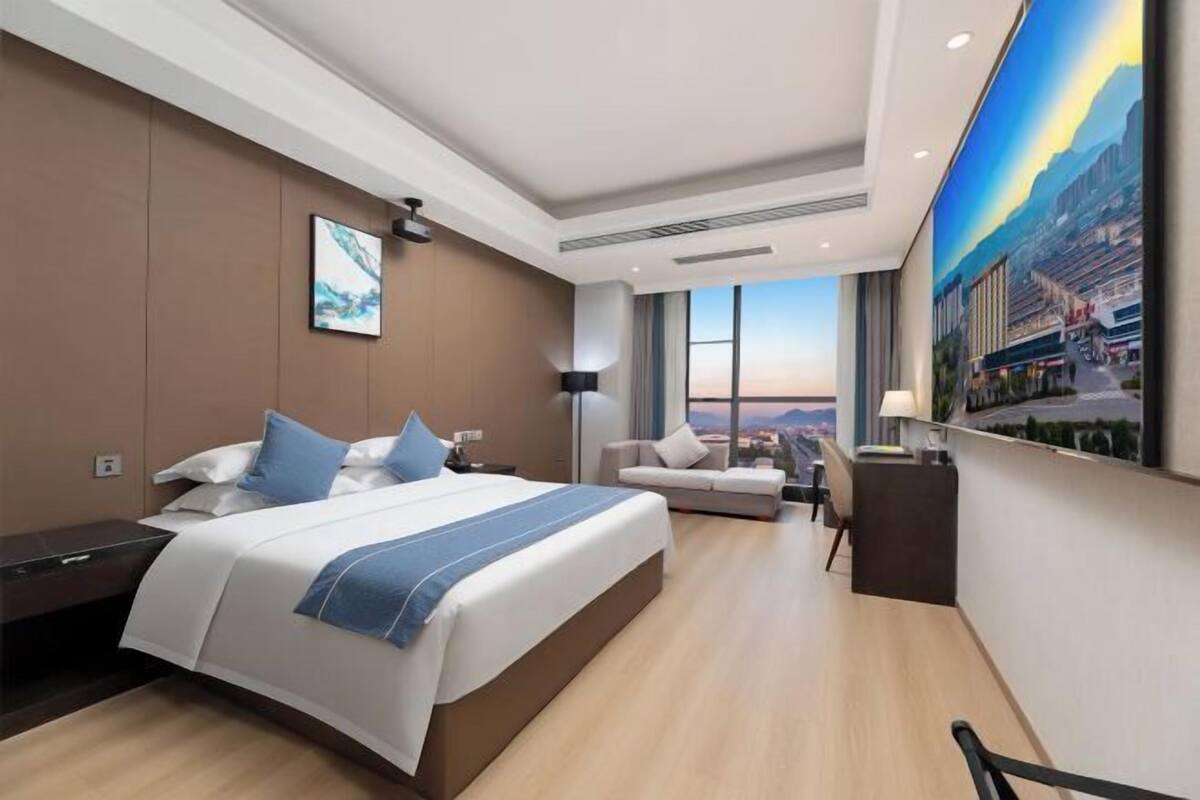 Ein modernes Hotelzimmer mit einem großen Bett, einem Schreibtisch, einer Sitzecke und einem großen Fenster mit Blick auf die Stadt.