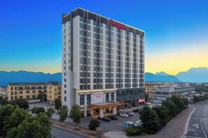 Un hôtel à plusieurs étages, doté d’une façade moderne, d’un parking et offrant une vue sur les montagnes en arrière-plan.