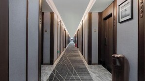 A hotel hallway with a patterned carpet, wooden doors, and a trash can. - Ramada by Wyndham Zhangjiajie (Zhangjiajie)