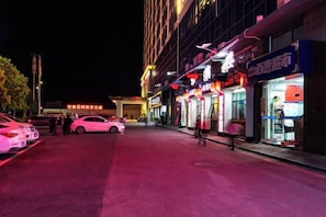 Eine beleuchtete Straße bei Nacht mit parkenden Autos und leuchtenden Schaufenstern.