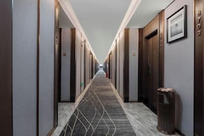A hotel hallway with doors on both sides, a patterned carpet, and a trash can on the right. - Ramada by Wyndham Zhangjiajie (Zhangjiajie)