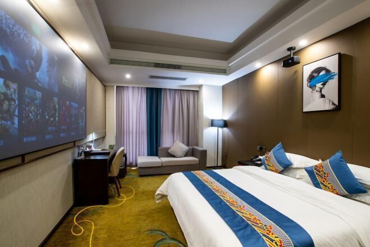 Ein Hotelzimmer mit einem großen Bett, einem Schreibtisch, einer Sitzecke und einer Projektionsleinwand, die Bilder zeigt.