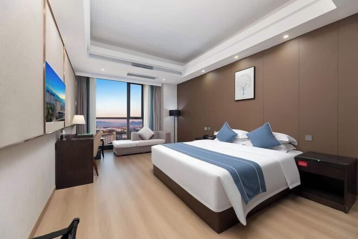 Ein modernes Hotelzimmer mit einem großen Bett, einem Schreibtisch, einer Sitzecke und Blick auf die Stadt.