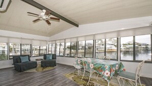 A spacious room with a dining table, two sofas, and a ceiling fan. Large windows offer views of a body of water and buildings. - Laughing Gull House, Laughing Gull House (Wakulla County)