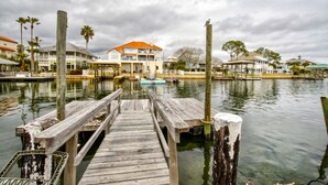 A wooden dock leading to a marina with boats, a large house with a red roof, and palm trees. - Laughing Gull House, Laughing Gull House (Wakulla County)