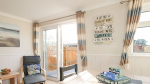 A room with a table set for dining, a chair with a cushion, a window with curtains, and a wall with a decorative sign. - Milton House (Weymouth)