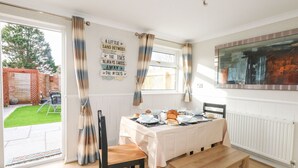 A dining area with a table set for a meal, a bench, and a view of the garden through a glass door. - Milton House (Weymouth)