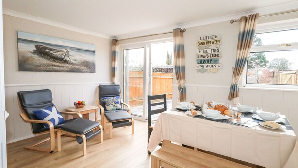 A dining area with a table set for four, two chairs, a bench, and a painting of a boat on the wall. - Milton House (Weymouth)