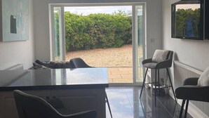 Cozinha moderna com uma ilha grande, banquetas de bar e vista para um jardim através de uma porta de vidro.