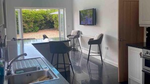 Cozinha moderna com uma ilha grande, área de jantar com banquetas, televisão na parede e vista para o exterior.