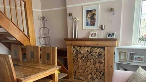 Uma sala de estar aconchegante com escada de madeira, lareira com parede de troncos, mesa de jantar e sofá com almofada.
