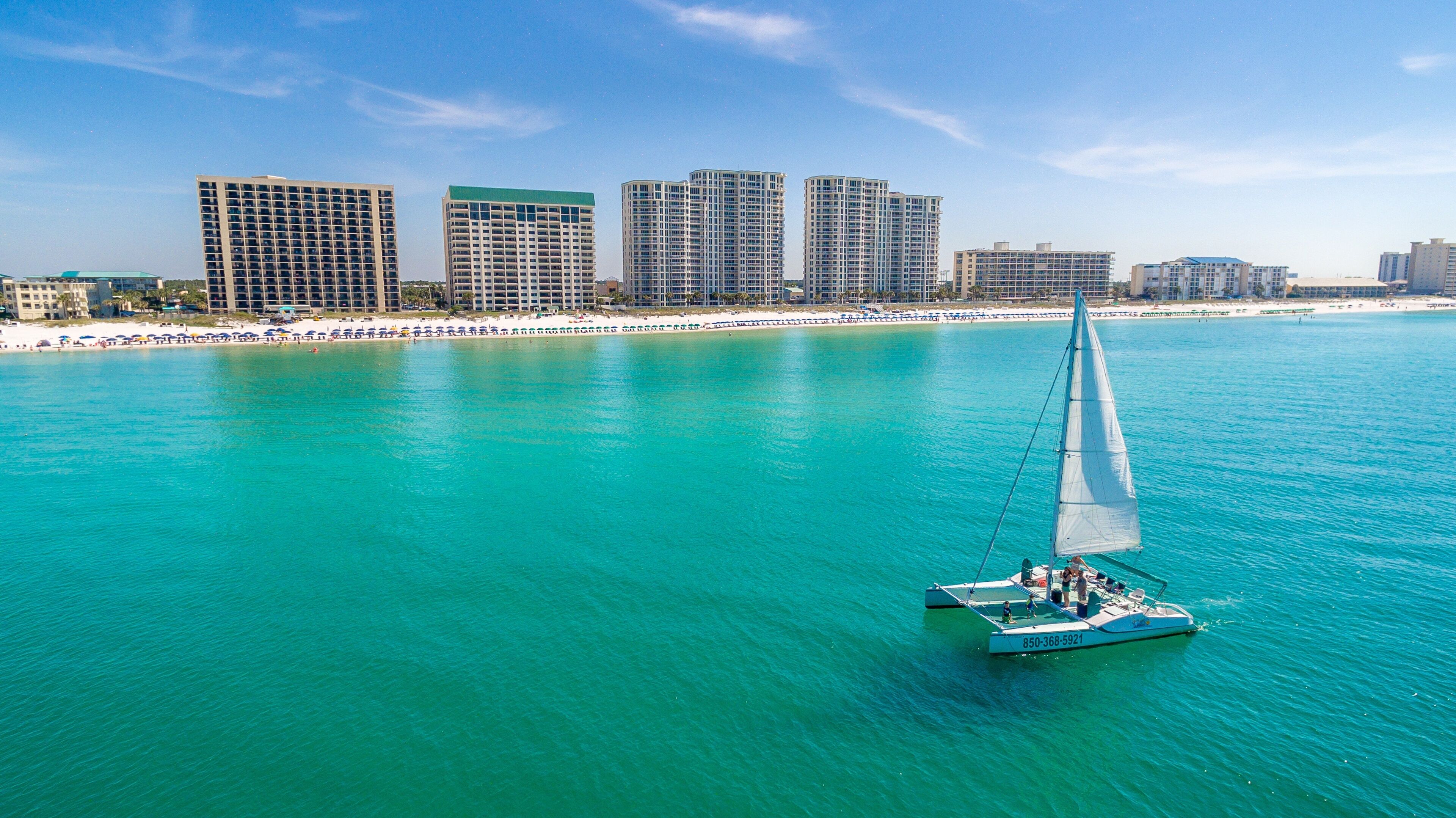 A sailboat on turquoise waters with a city skyline in the background.