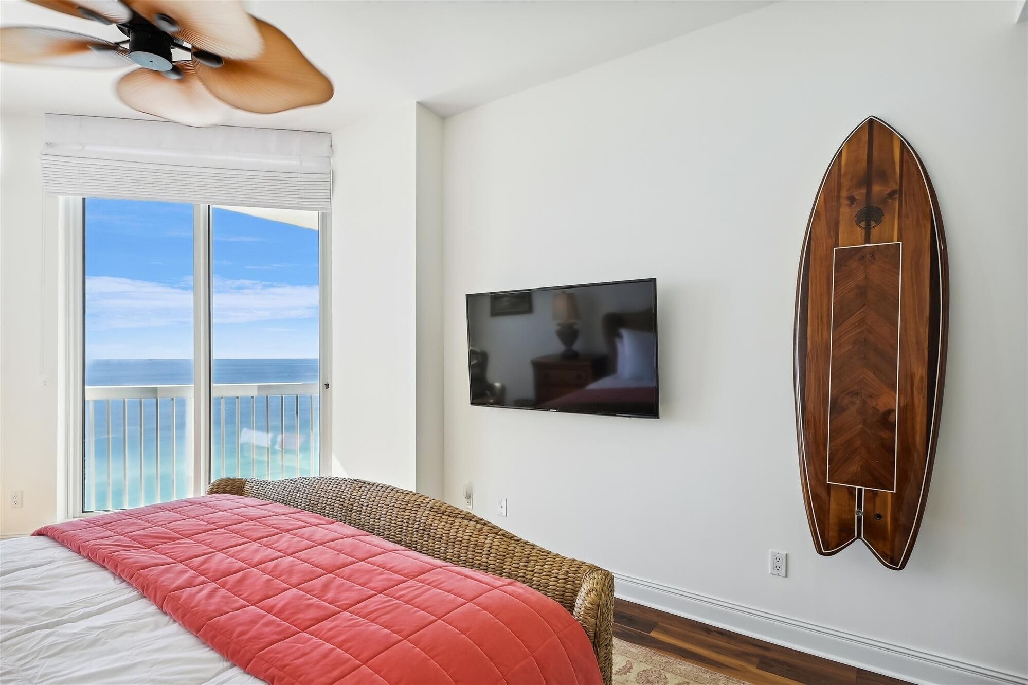 Ein Schlafzimmer mit einem großen Bett, einem Fernseher, einem Surfbrett und einem Balkon mit Meerblick.