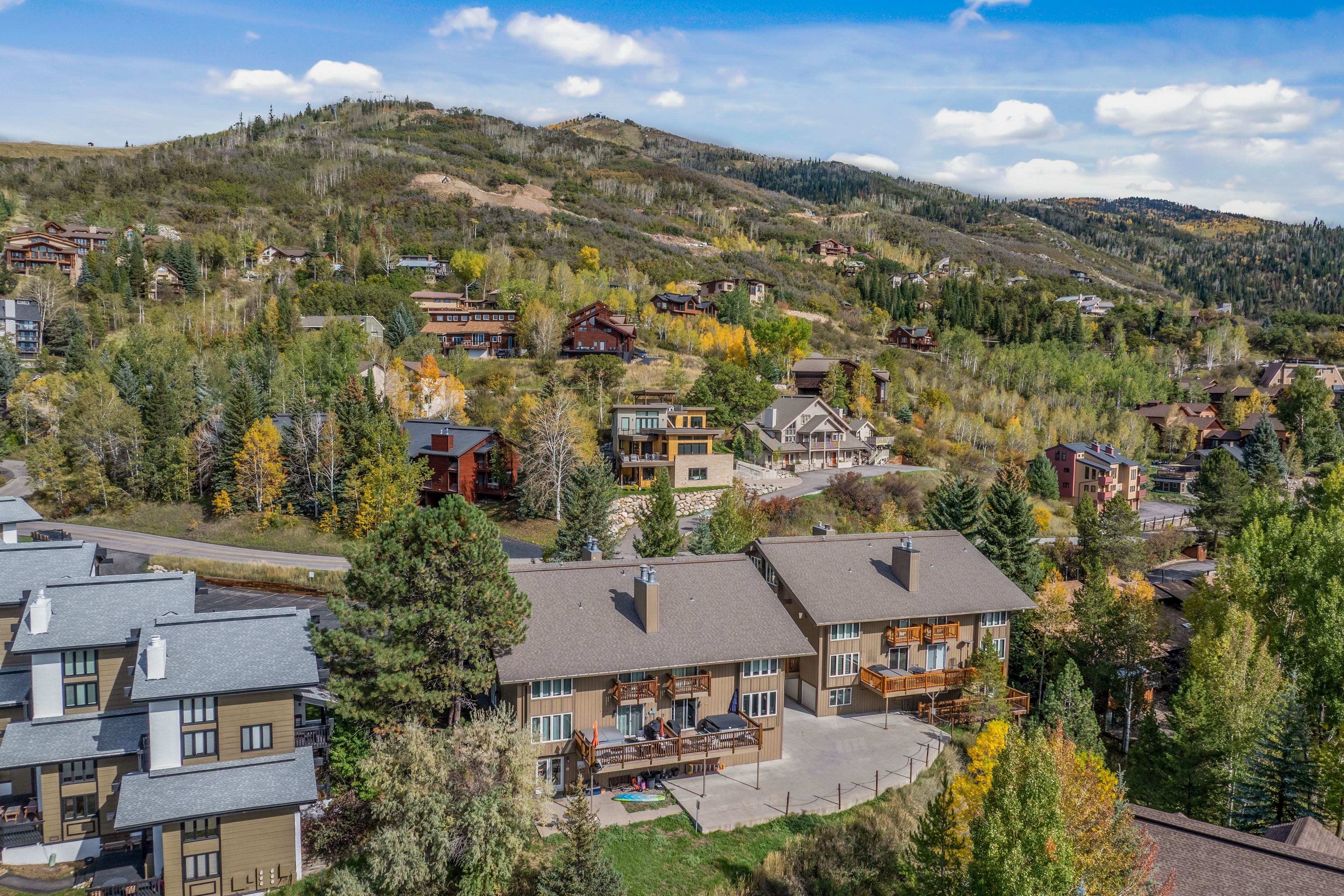 A residential area with multiple houses, some with balconies, surrounded by trees and hills.