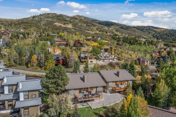 A residential area with multiple houses, some with balconies, surrounded by trees and hills.