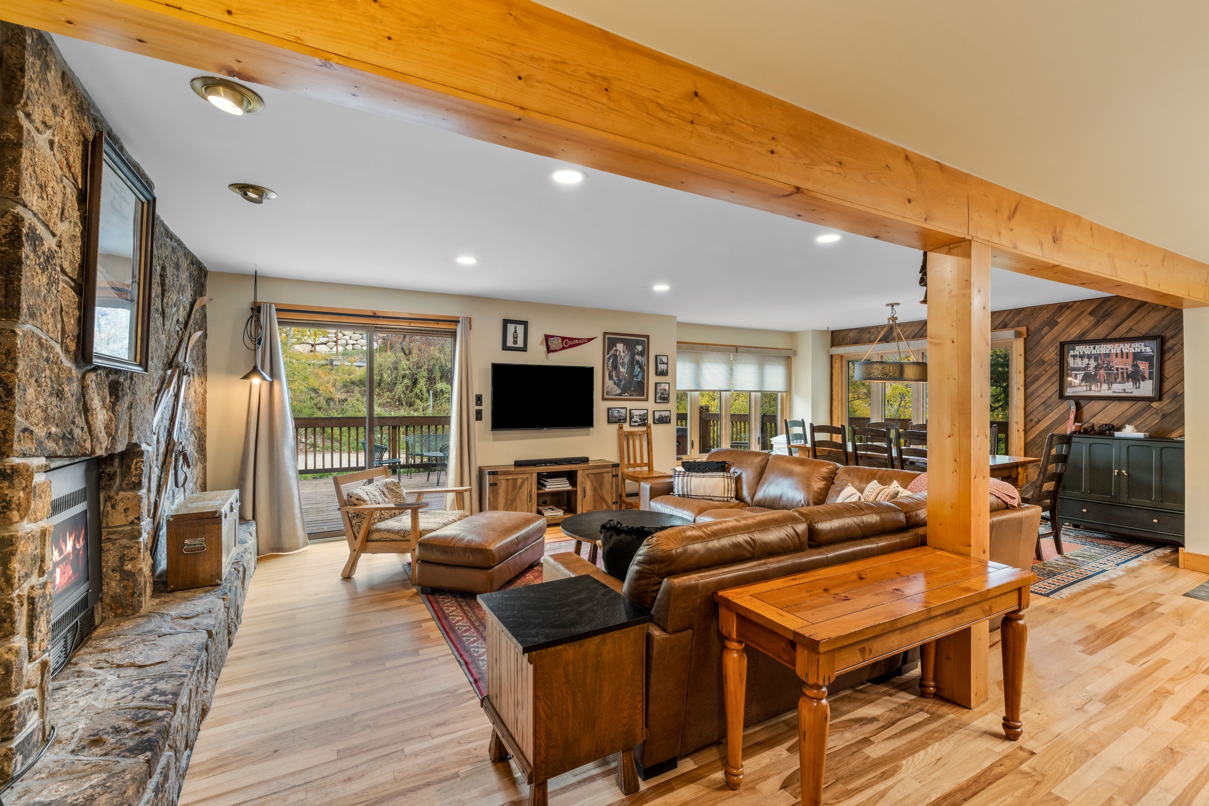 Un salon spacieux avec une cheminée en pierre, un canapé en cuir, une table à manger en bois et un téléviseur fixé au mur.