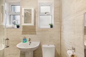 A bathroom with a sink, toilet, and two windows with plants. - Modern 4BR Victorian Home Near Luton Airport (Luton)