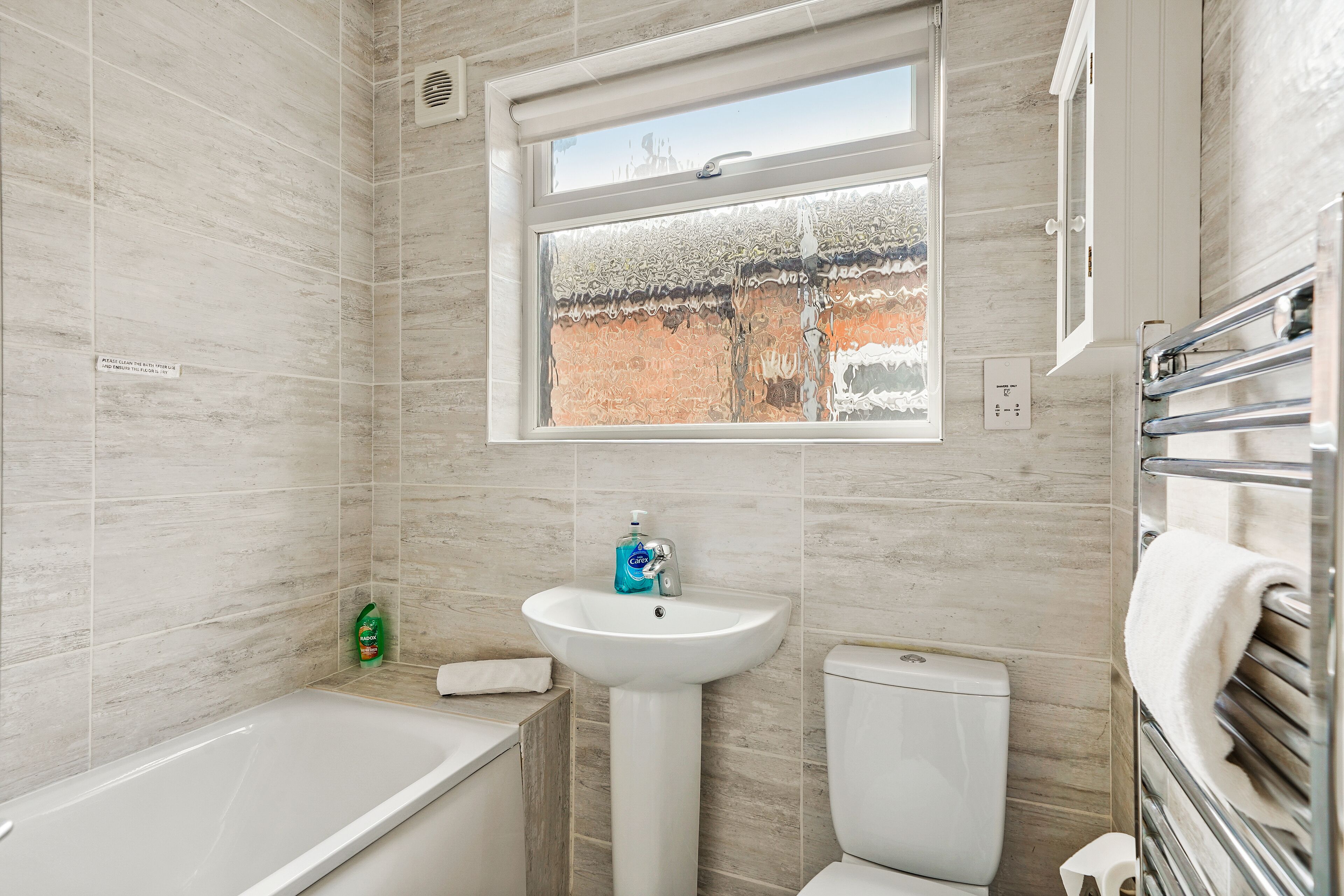 A bathroom with a bathtub, sink, and toilet, featuring a window with a view of a building outside.