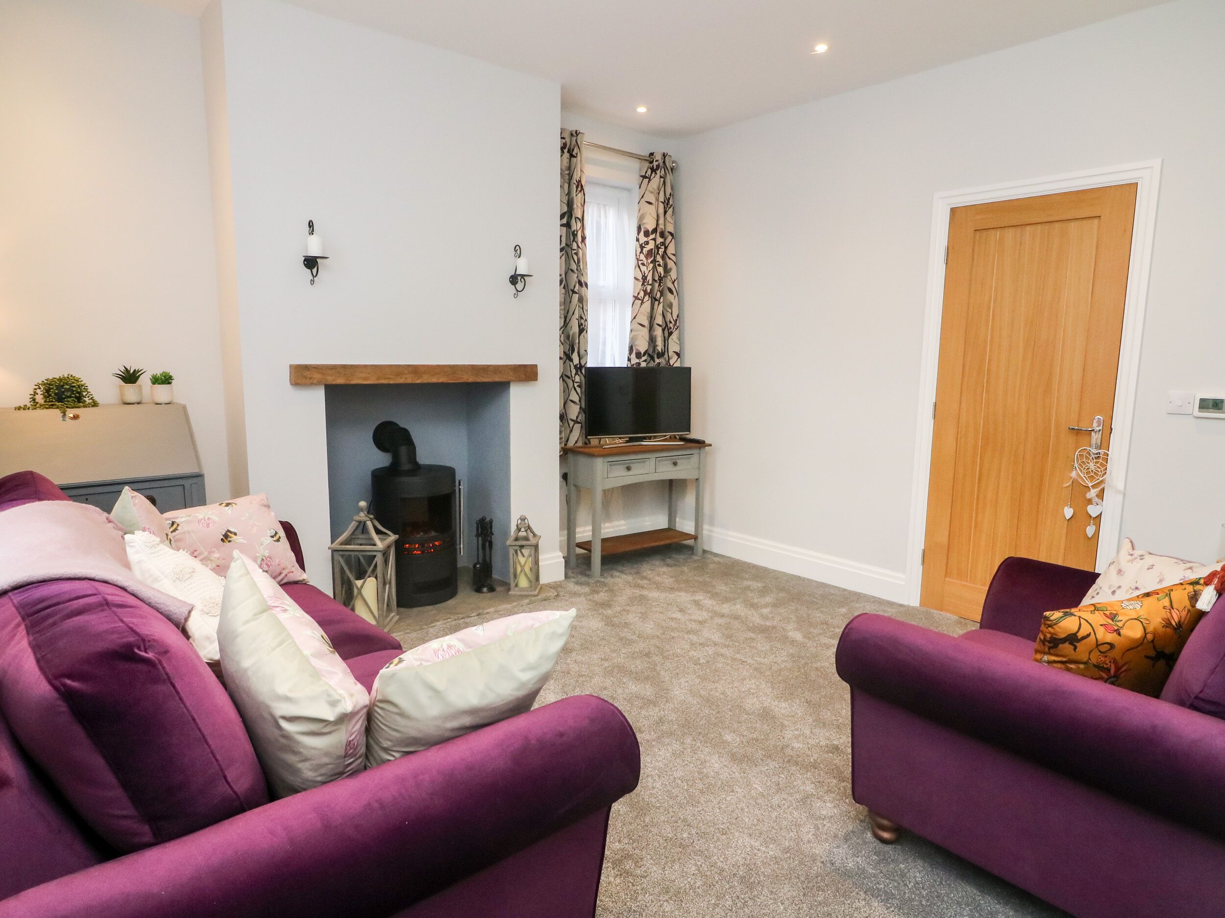 A living room with purple sofas, a fireplace, a television on a stand, and a door.