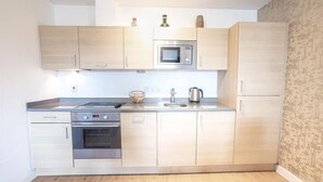 Une cuisine moderne avec des meubles en bois clair, un four à micro-ondes en acier inoxydable, un four encastré et un évier.