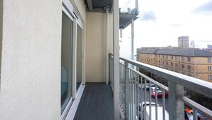 Un balcon doté d’une rambarde en métal, donnant sur un parking et sur des bâtiments situés au loin.