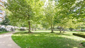 Un parc avec un chemin pavé, de l’herbe verte et des arbres.