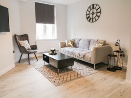 Una sala moderna con un sofá, una mesa de centro, una silla, un reloj y una ventana con persianas.