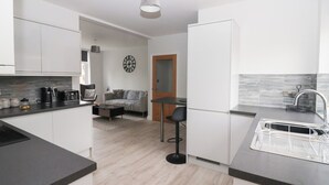 Una cuina moderna amb armaris blancs, un taulell negre i una porta de fusta que dona a una zona d'estar.