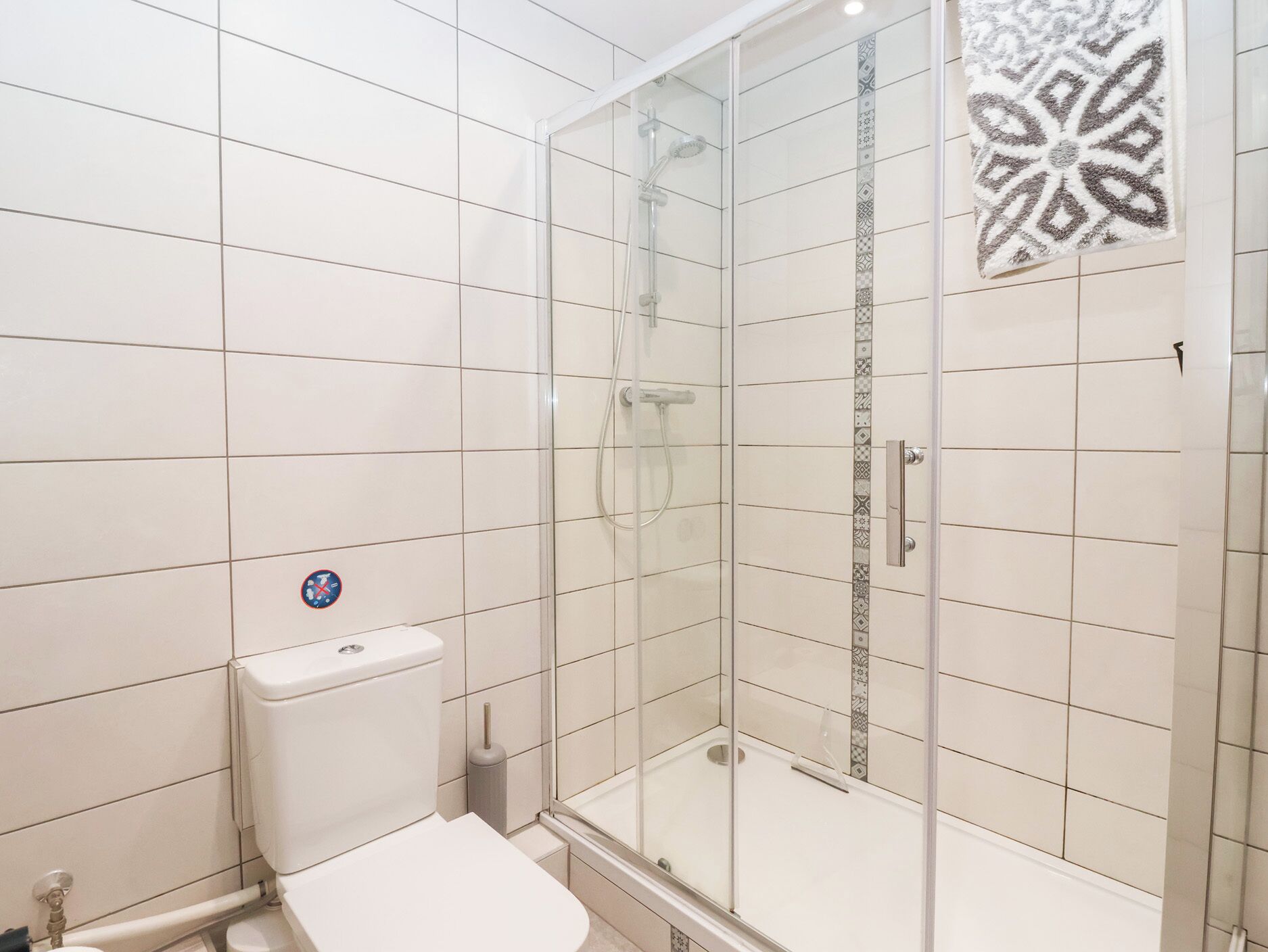 A modern bathroom with white tiles, a glass shower enclosure, a toilet, and a bidet.