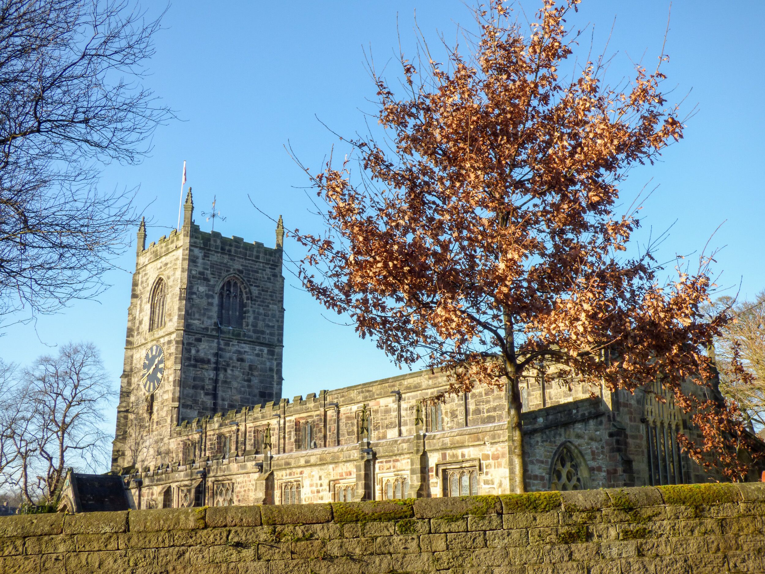 A historic stone building with a clock tower, large windows, and a moss-covered wall.