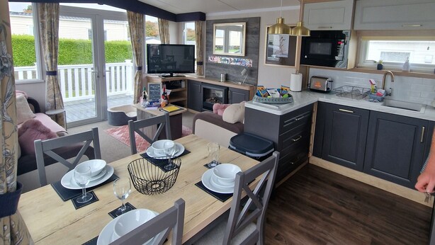 A modern kitchen with a microwave, sink, and dining area with a table set for four. - 8 Birth Static Caravan (Filey)