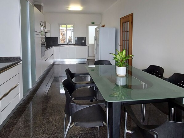 A modern kitchen with stainless steel appliances, a dining area with a glass table and black chairs, and a potted plant on the table.