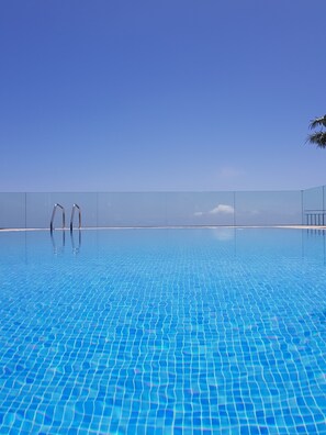 Une piscine aux eaux d’un bleu limpide, dont le fond est recouvert de carreaux, entourée d’une clôture et surplombée par un ciel dégagé.