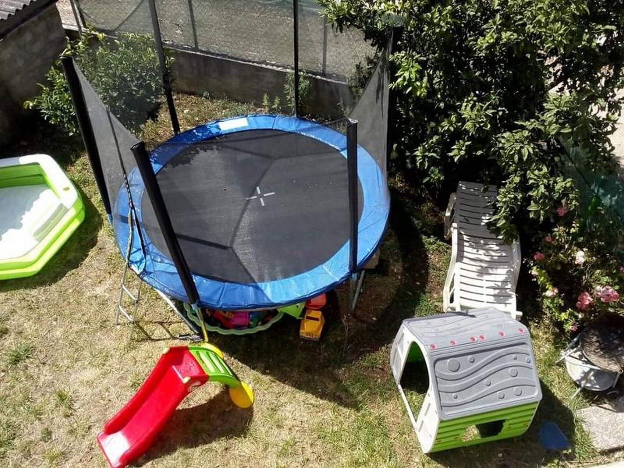 Een trampoline omringd door een gazon met een kleine glijbaan en een huisje voor een huisdier.