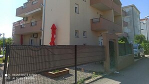 Un edificio residenziale a più piani con balconi, un ingresso chiuso da cancello e un oggetto rosso a terra.