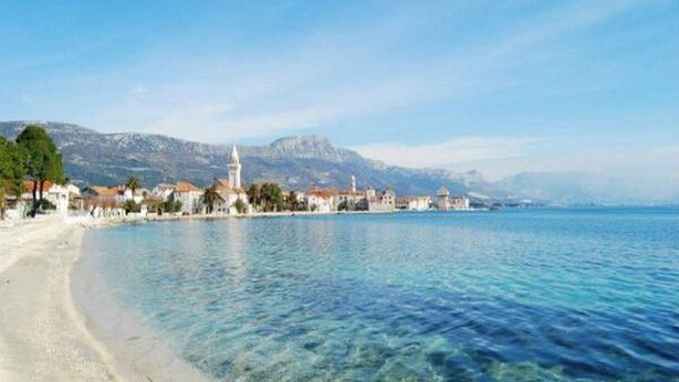 Una località costiera con acque cristalline, una spiaggia sabbiosa e edifici lungo la riva.