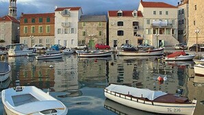 Una marina con barche ormeggiate, un edificio in pietra con tetto rosso e una torre sullo sfondo.