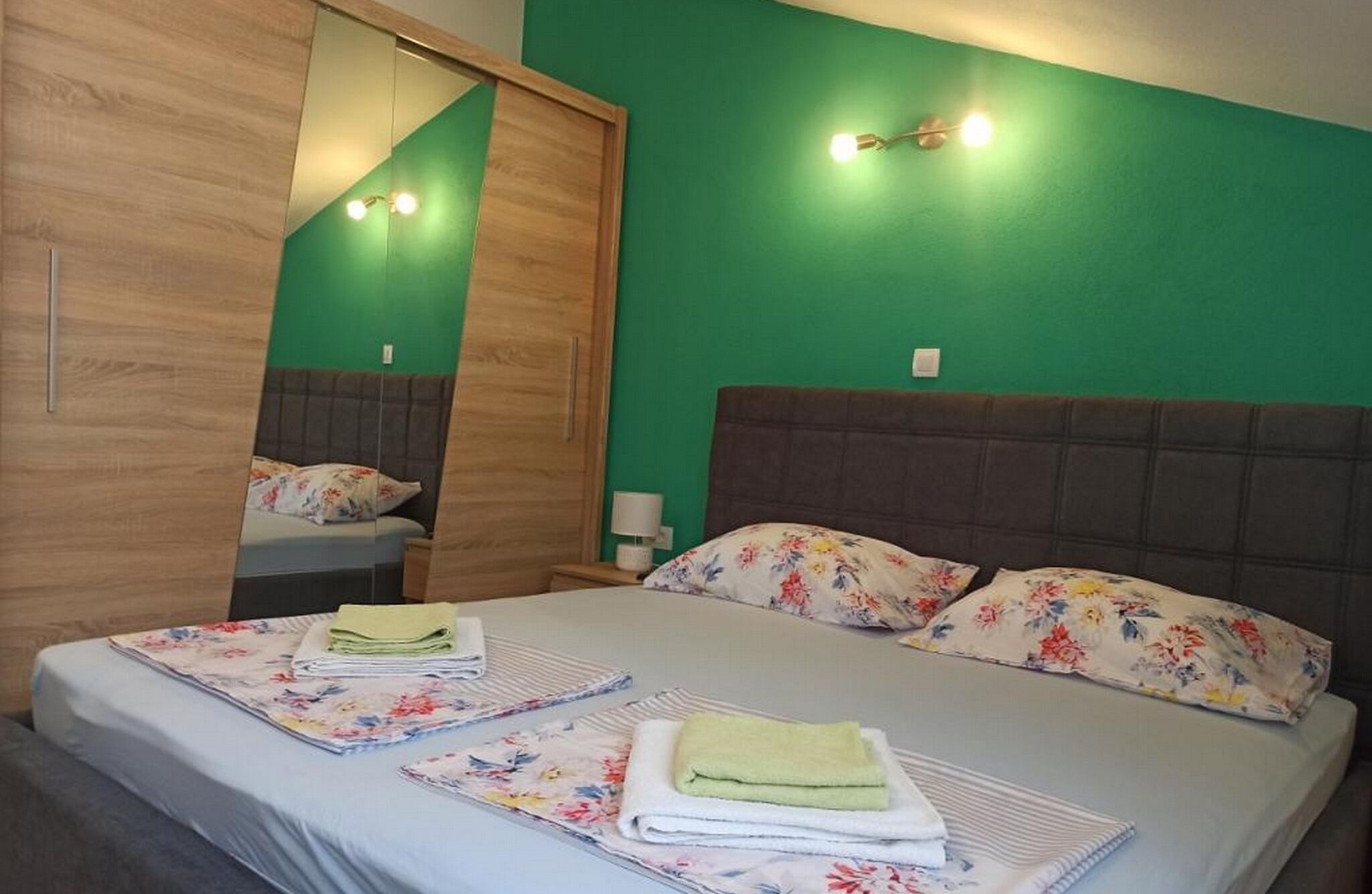 Ein Schlafzimmer mit einem Bett, zwei Nachttischen, einem Spiegel und einer grünen Wand.