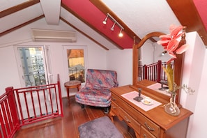 Relax in a charming room with a sloped ceiling, wooden bench, and dresser, offering a balcony with a railing.