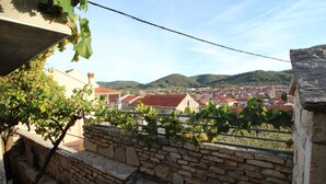 A stone wall with a vineyard in the foreground and a town with red-roofed buildings in the background.