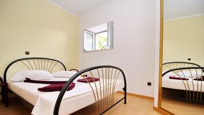 A single bed with a metal frame, white bedding, and a small window above it.