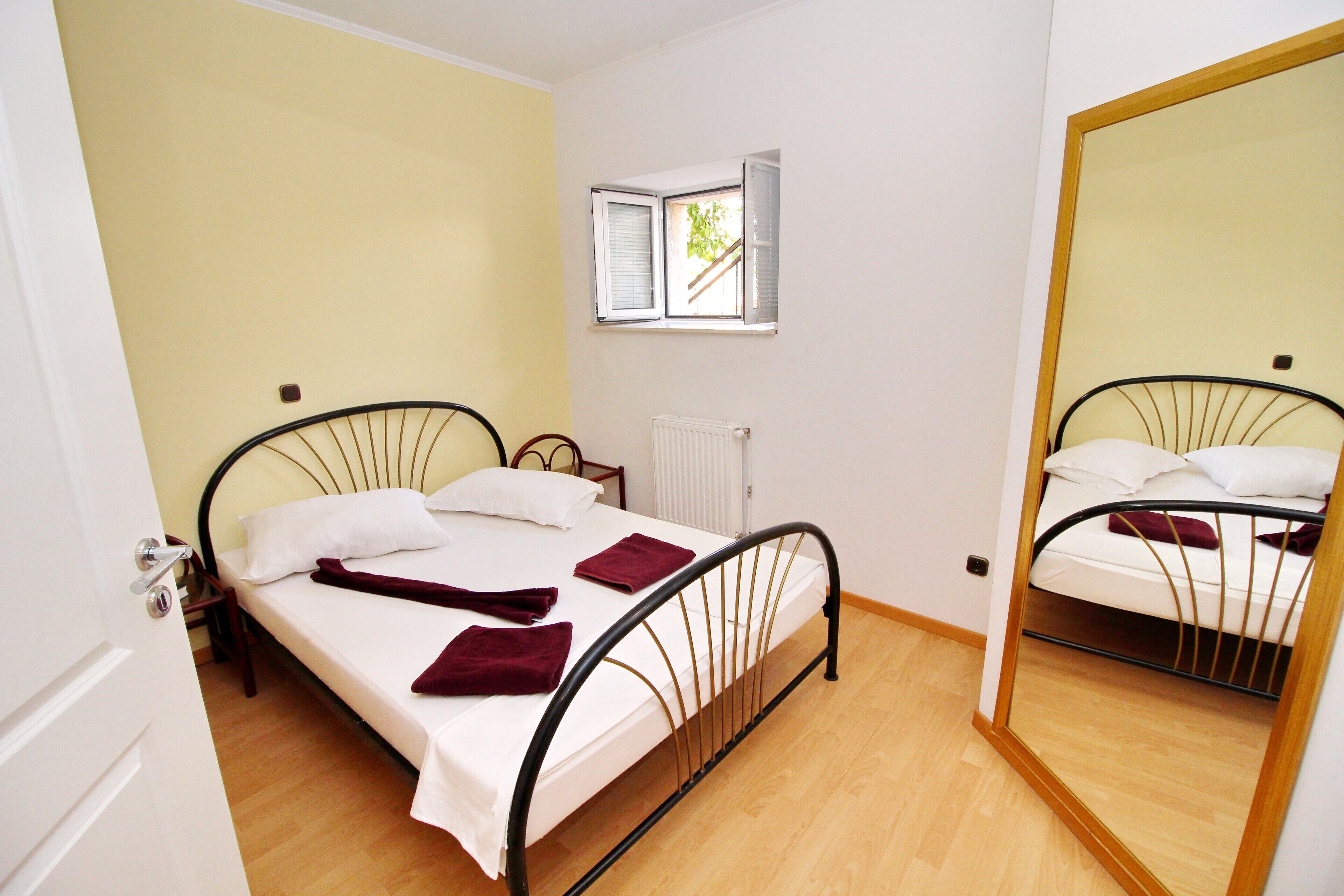 Un lit simple avec une tête de lit, une fenêtre avec des stores, un radiateur et un miroir.