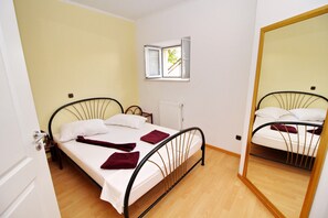 Uma cama de solteiro com cabeceira, janela com persianas, radiador e um espelho.