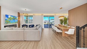 A modern living room with a large sectional sofa, a dining area with a wooden table and white chairs, and a staircase with a black railing. - Private Pool Home with Awesome Game Room-9270SHD (Davenport)