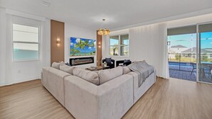 A modern living room with a sectional sofa, a flat-screen TV, a fireplace, and a large window offering a view of the outdoors. - Private Pool Home with Awesome Game Room-9270SHD (Davenport)