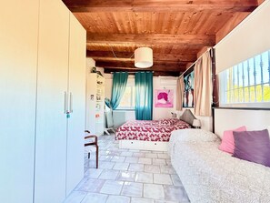 A bedroom with a wooden ceiling, a bed with patterned bedding, a chair, a wardrobe, and a window with curtains. - Vesuvio Country House (Campania)