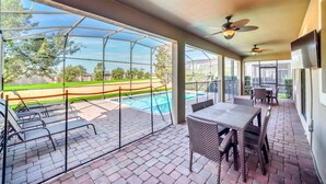 Un patio techado con piscina, muebles de exterior y ventiladores de techo.